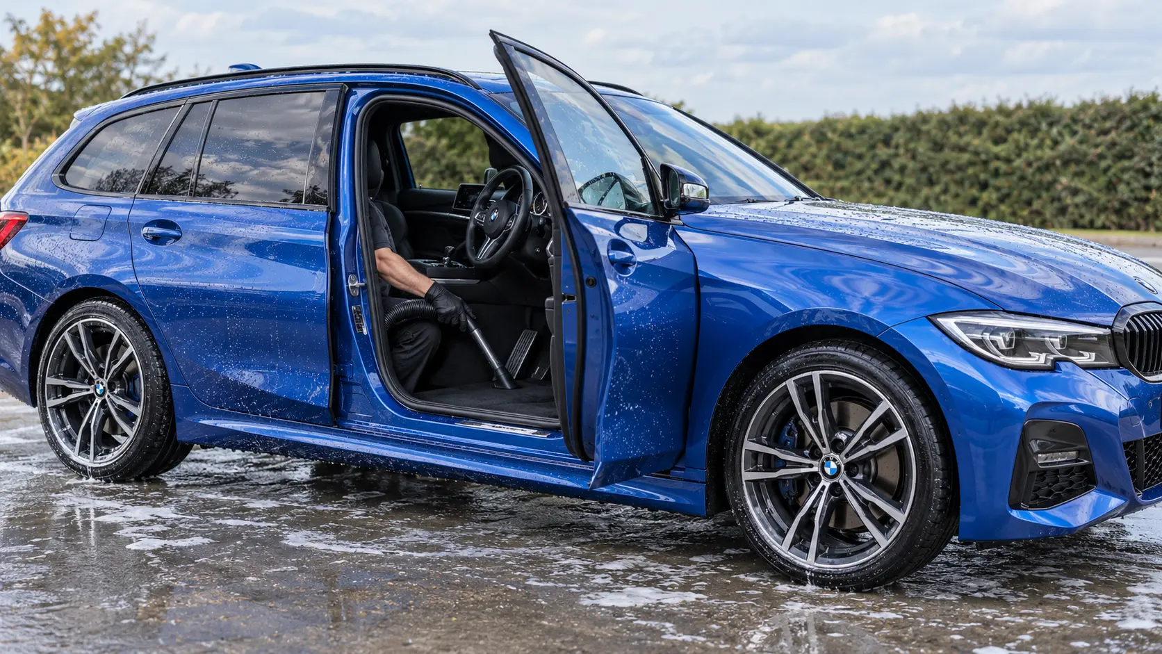 Right-hand-drive blue BMW 3 Series Touring receiving a hand wash and interior vacuum